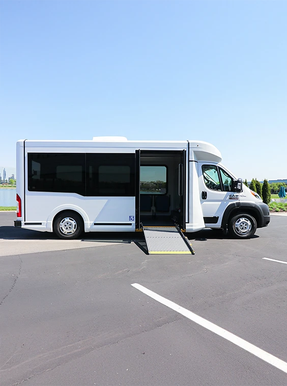 White shuttle accessible bus with blue sky and trees at a parking lot